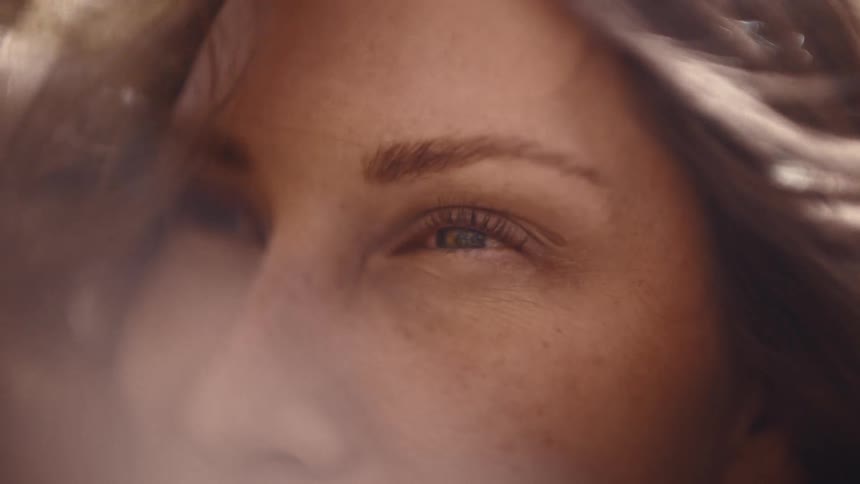 A very close view of a womans brown eyes and face in soft focus with her brown hair moving around her face