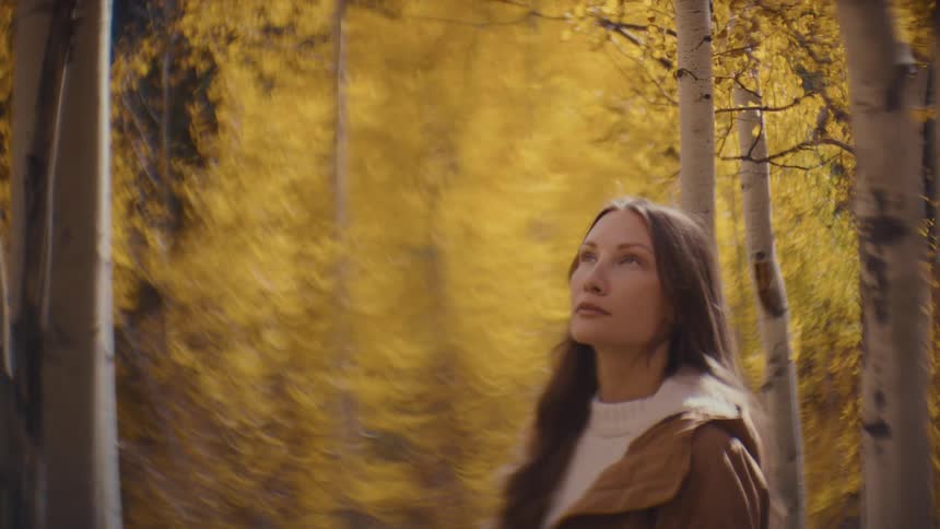 A woman gazes upward while standing in a forest of vibrant golden autumn trees
