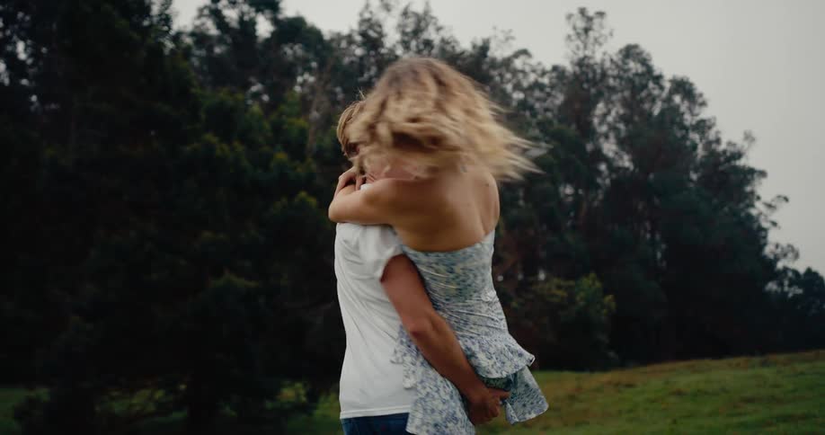 A happy couple runs toward each other embracing spinning and laughing in a wide green field surrounded by trees