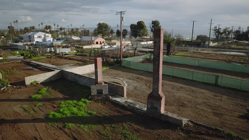 Vacant lot with remaining brick chimneys and a residential neighborhood in the background