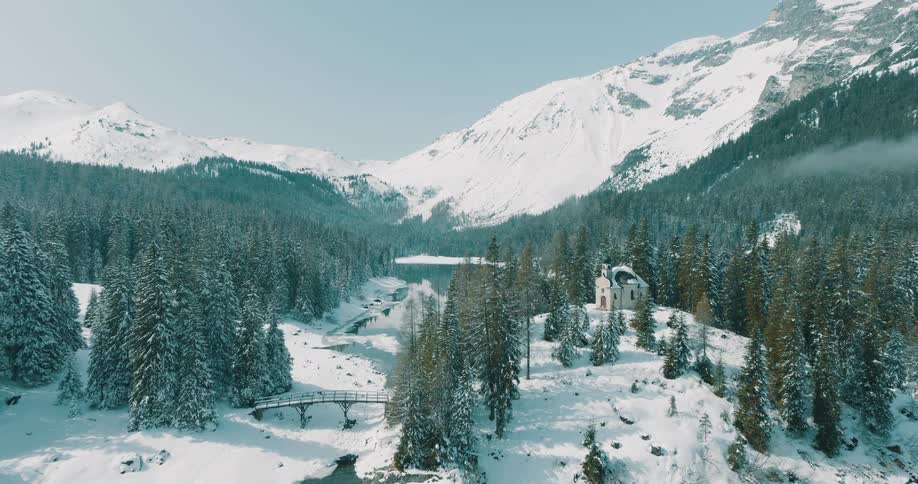 Aerial of a snow covered forest and frozen lake with a small chapel nestled among the trees