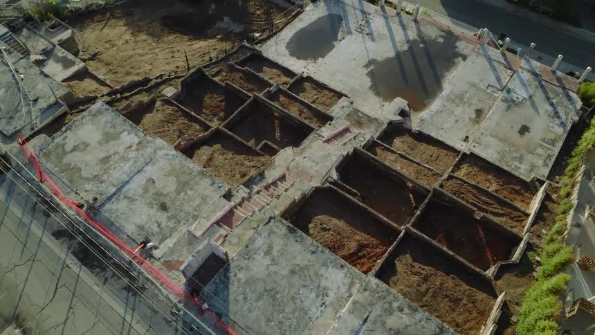 An overhead aerial view shows the foundation and excavated dirt holes for rooms on a construction site