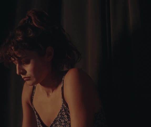 Woman sitting in front of a dark curtain looking to the side