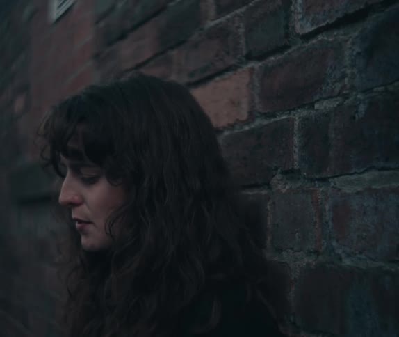 Woman smoking while leaning against a brick wall