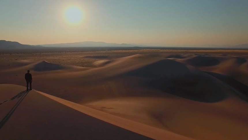 Man standing on top of a dune as sunlight shines on dunes across the desert