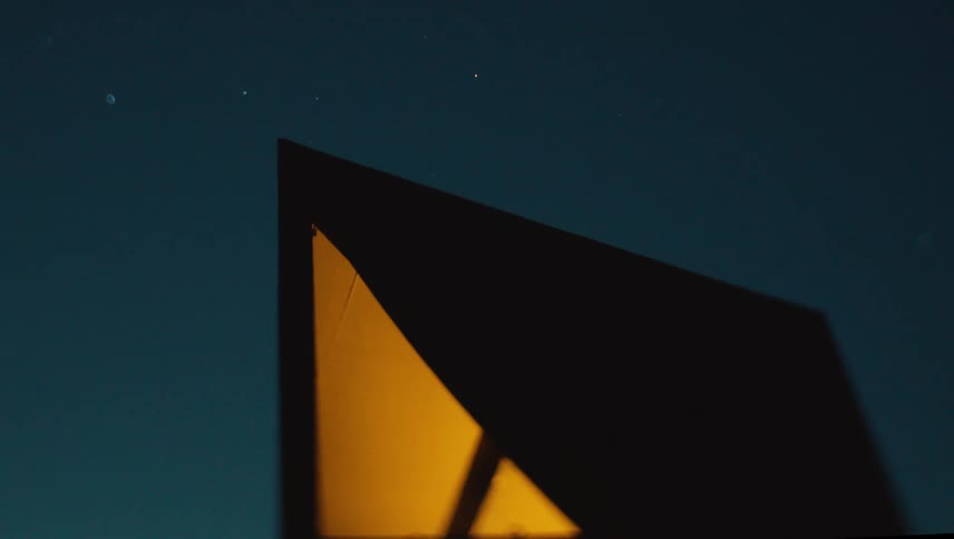 A brightly lit camping tent set against a starry night sky