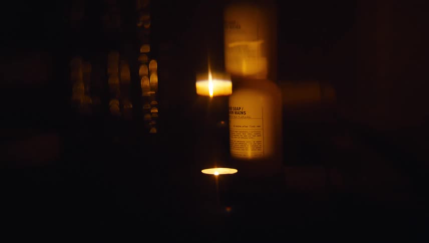 A small candle illuminates a nearby plastic bottle of hand soap