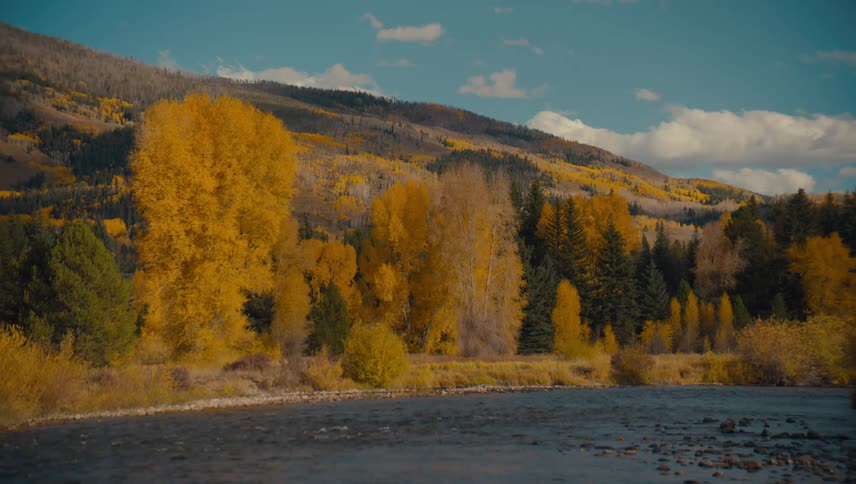 A river flows through mountains with golden and green autumn trees under a blue sky
