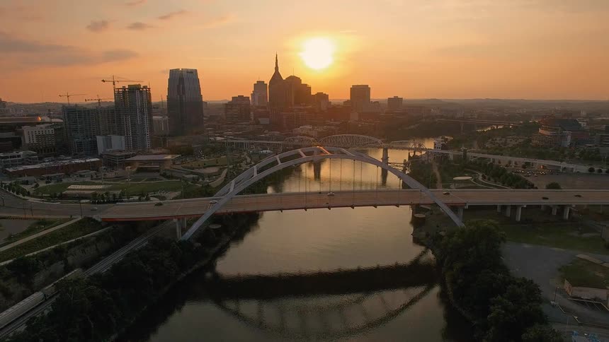 Arched bridge over a river with an urban skyline at sunset