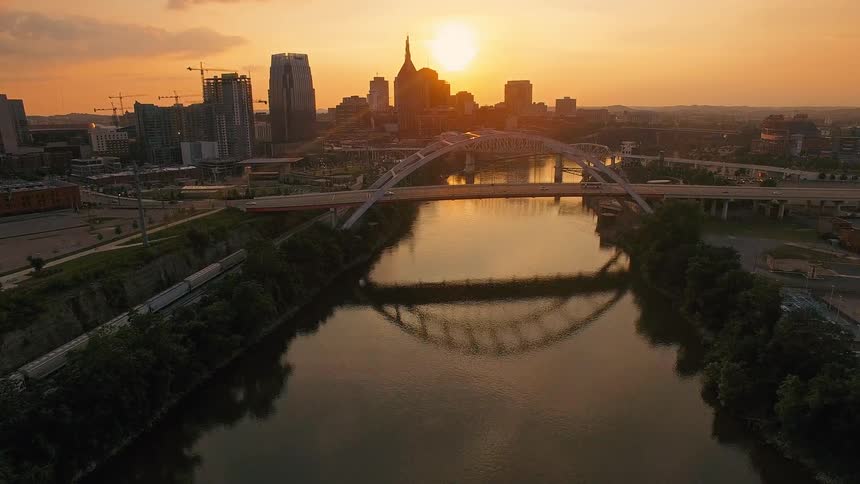 Arched bridge reflected in the river with an urban skyline at sunset