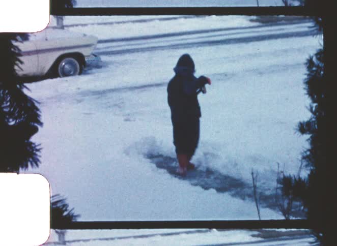 A person wearing red boots shovels snow from a driveway