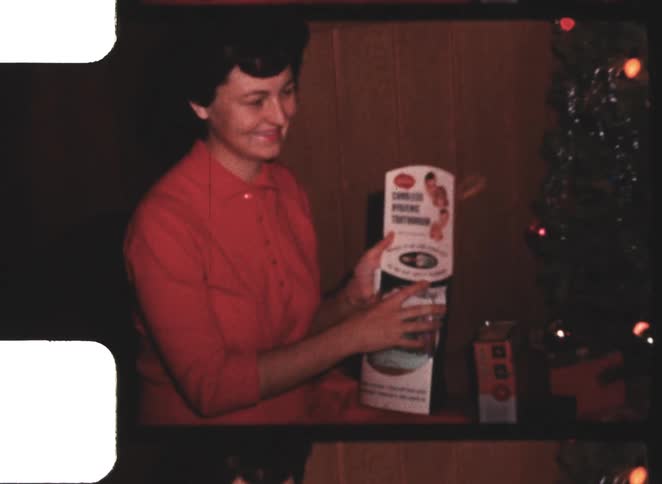 Woman wearing red clothes holds a box next to a christmas tree