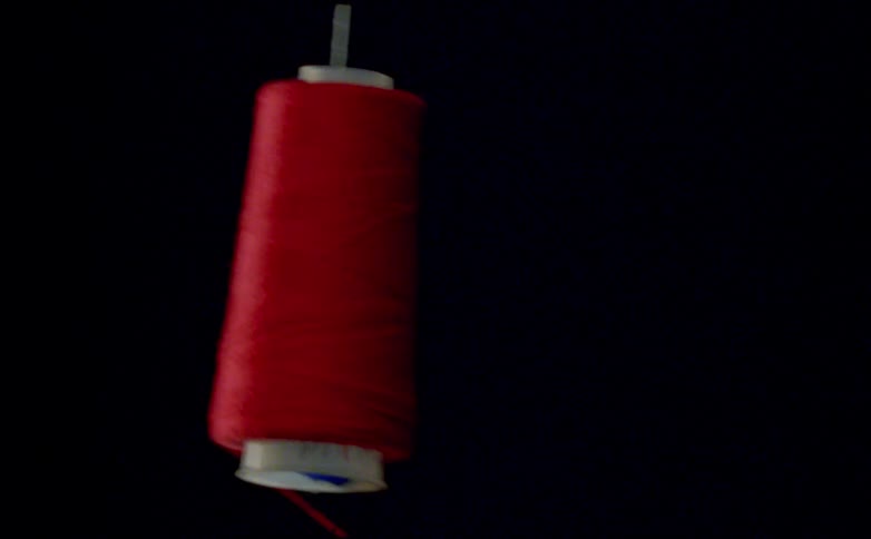 Close up of an unwinding red thread spool dangling in a red room