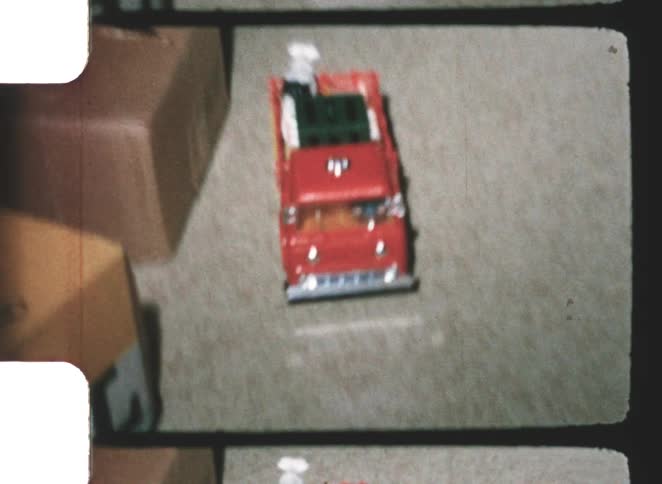 Vintage color video from the 1960s captures a red toy truck with small white figurines on its bed driving across a dark carpet