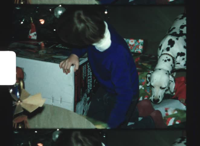 Child opens devils mountain challenge toy beside dalmatian among christmas presents