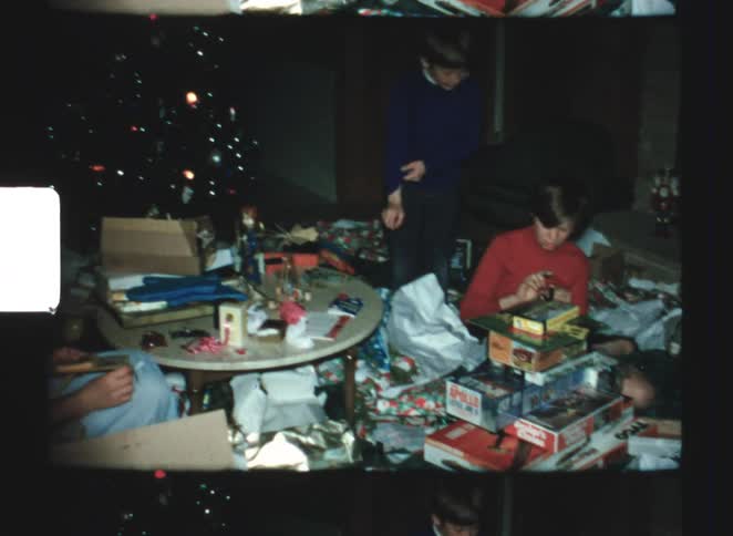 A family is gathered around the christmas tree as they open presents