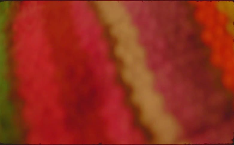 A macro perspective traces the vertical multicolored stripes of a knitted blanket capturing the fibrous detail of the yarn before the view softens into an abstract blur
