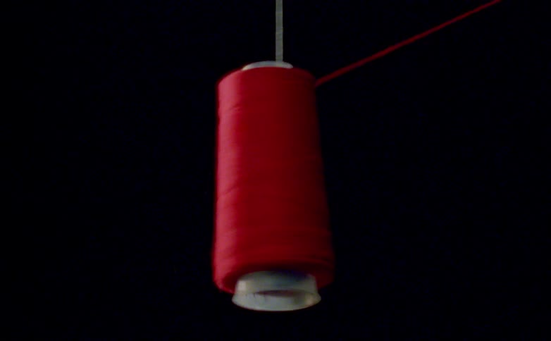 A red sewing thread spool dangling in the air from a rope