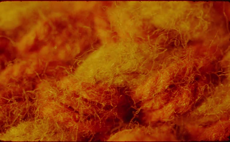 A close view shows warm bright orange and yellow textured crochet or woven material that fades in and out of focus with cinematic grain