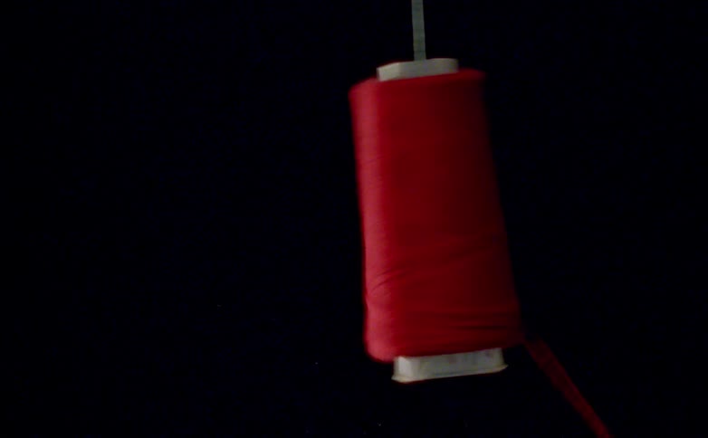 Red thread spool suspended against black background with strand extended horizontally
