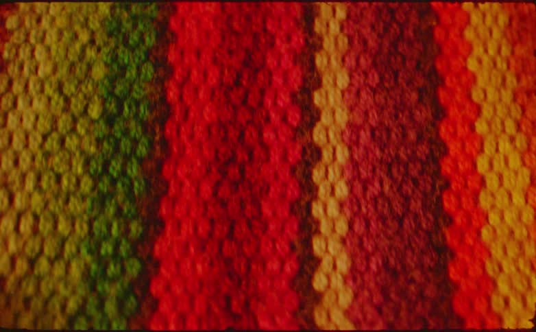 This is a closeup shot of a densely knitted or woven textile with distinct vertical stripes of color the vibrant stripes feature a color pattern including green yellow red maroon and orange suggesting a blanket rug or shawl