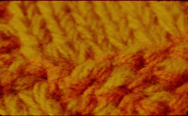 This video is a closeup of a knitted or crocheted textile possibly a blanket or scarf the yarn is a blend of warm vibrant colors predominantly yellow gold and orange showing a distinct vshaped stitch pattern
