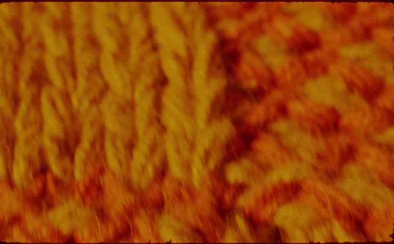 A close view of chunky yellow and orange knit yarn texture with a moving blur effect and a vintage film border