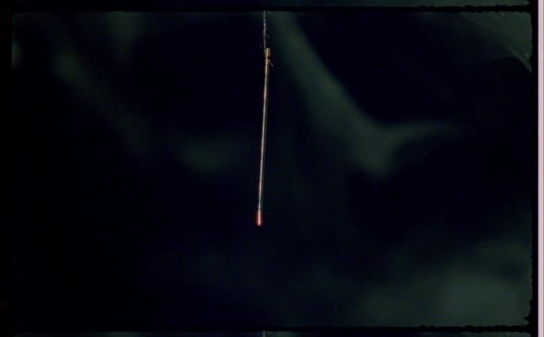A close view of a stick hanging down in a dark atmosphere surrounded by wisps of smoke