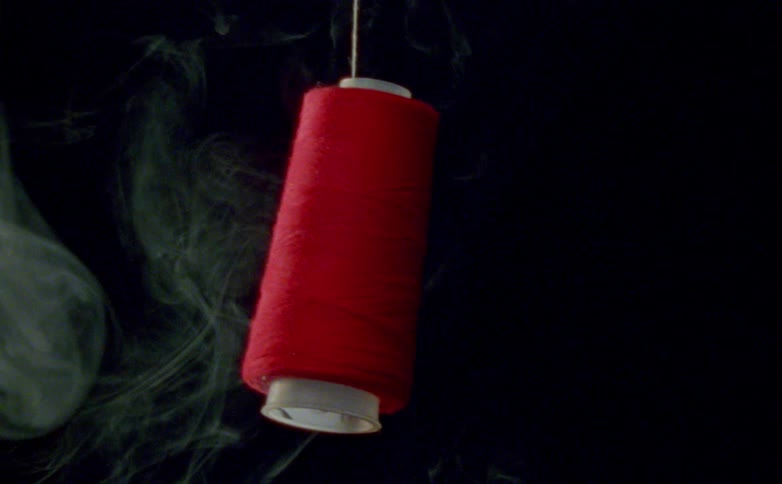 Closeup of a red thread spool hanging against a smoky background