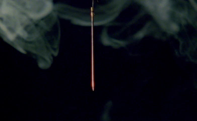 A close view of a stick dropping hanging down in a dark atmosphere surrounded by wisps of smoke
