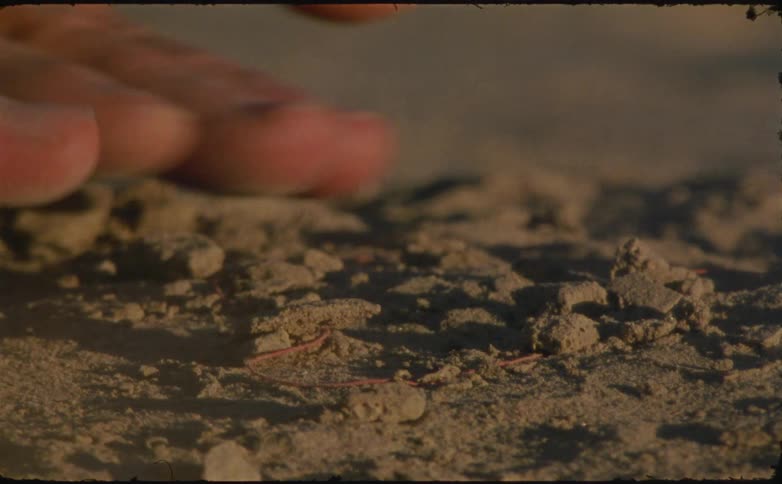 Hand removing a red thread from the sand