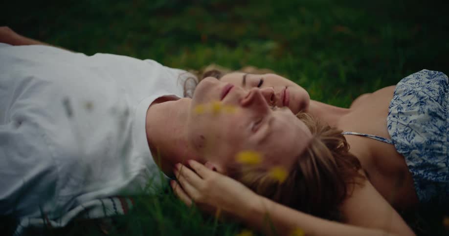 Couple lying on grass face each other as one gently touches the others head