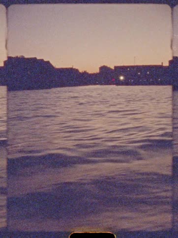 Gentle waves reflect orange sky in front of silhouetted city at dusk