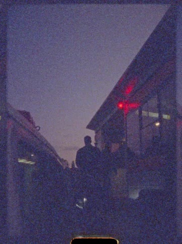 A group of people walks toward a building in the evening the fading light casting long shadows as they head inside