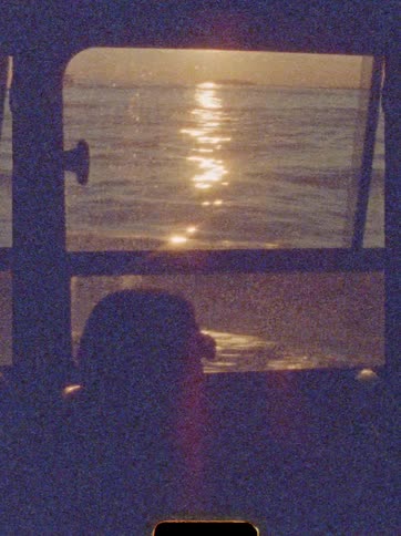 Silhouetted head watches sunset reflected on water through vehicle window
