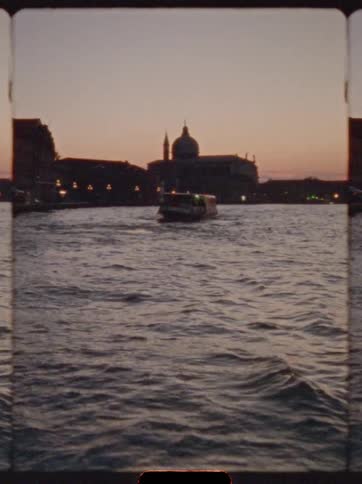 Boat sails at sunset through canal with silhouetted cathedral in the background