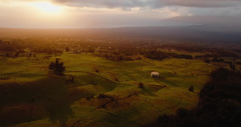 Wide rural landscape with green fields scattered structures and low sunlight on the horizon