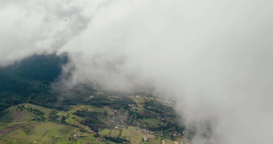 Rural landscape with green areas and small buildings partially covered by low clouds