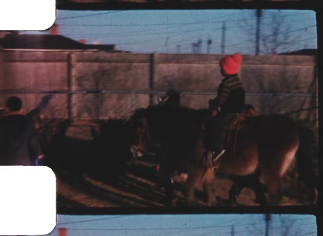 Boy rides a equid in the backyard as another boy leads the animal on a winter day