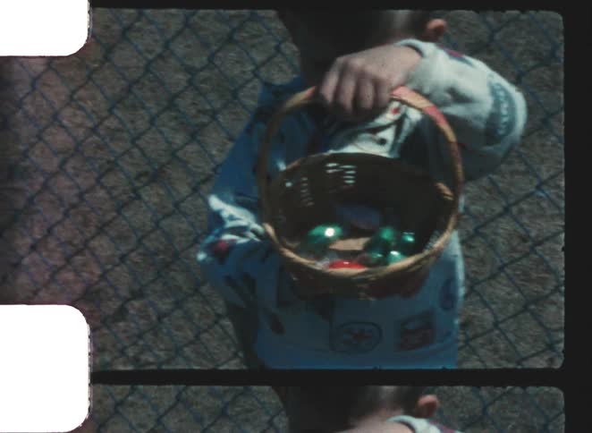 Boy standing near a chain link fence on an autumn day holds a basket full of colorful objects