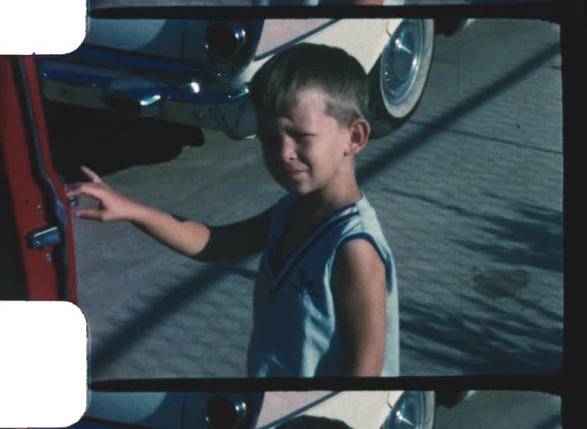Child standing on the street holding the open door of a parked car