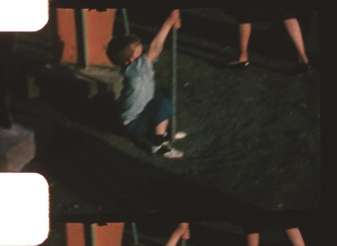 Child climbing down from a metal pole in an outdoor area with adults in the background