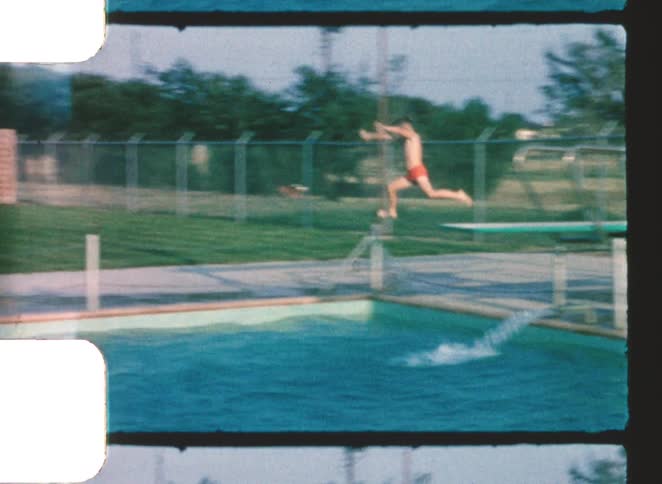 A young boy jumps from a diving board into a swimming pool