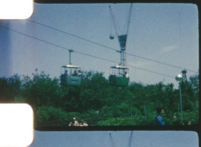 Cable cars operating above a wooded area with towers in the background