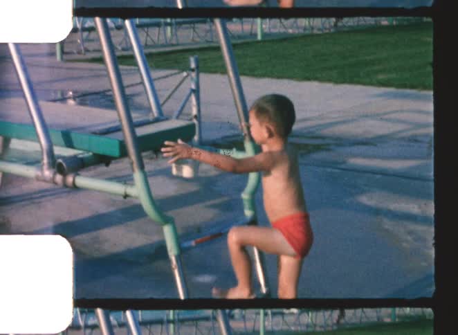 A young boy climbs the diving board ladder at a public swimming pool