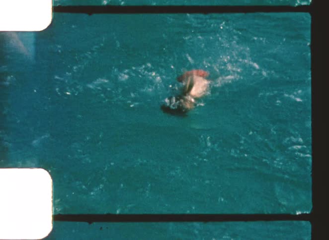 A boy jumps into a swimming pool at midday then swims across it excitedly under the bright sun