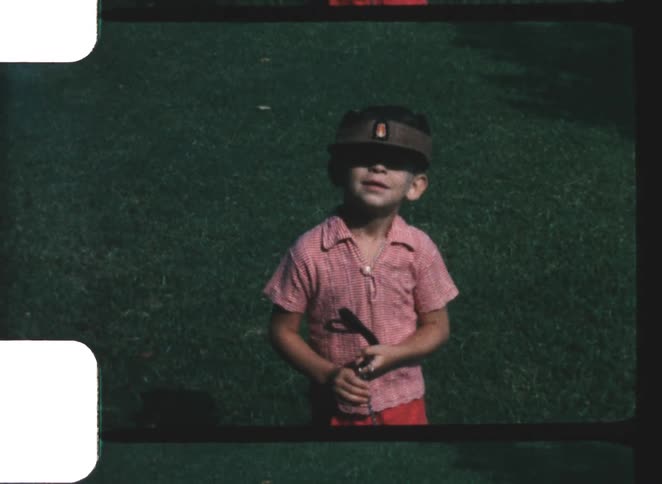 A young boy wearing a cap and a plaid shirt standing in green grass