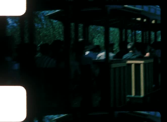 A group of children stands at a terminal at midday watching a passing train filled with people as it rolls by