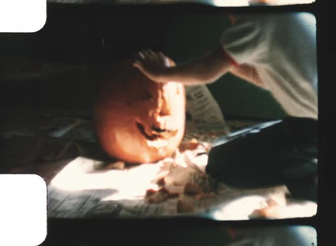 A kid carving a pumpkin into a face while indoors at midday