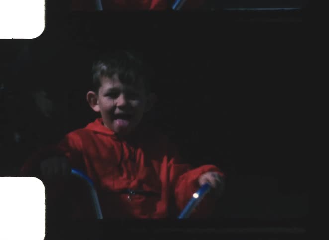 A kid in a red jacket riding a bike excitedly across the sidewalk at midday
